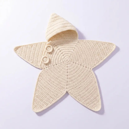 A cream-colored crocheted star-shaped baby blanket with a hood and two decorative buttons, displayed on a light lavender background.