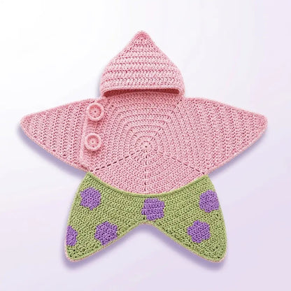 A crocheted star-shaped baby hat or bonnet with a pink top section, two pink buttons, and a green lower section with purple polka dots, shown on a plain light background.